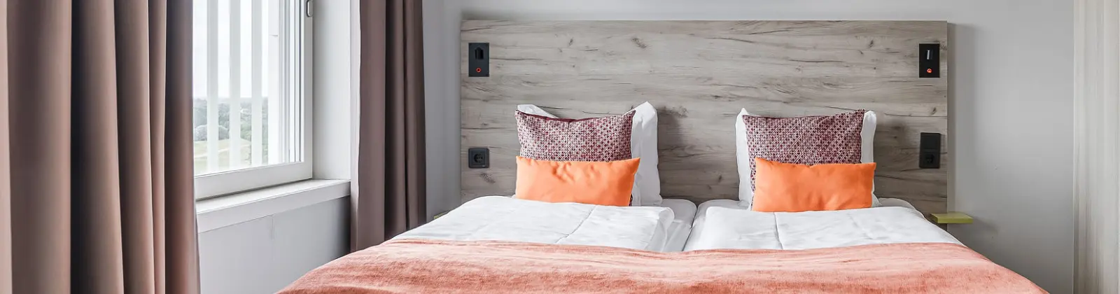 Modernt hotellrum med dubbelsäng, ljus sänggavel och ljusorange accenter.