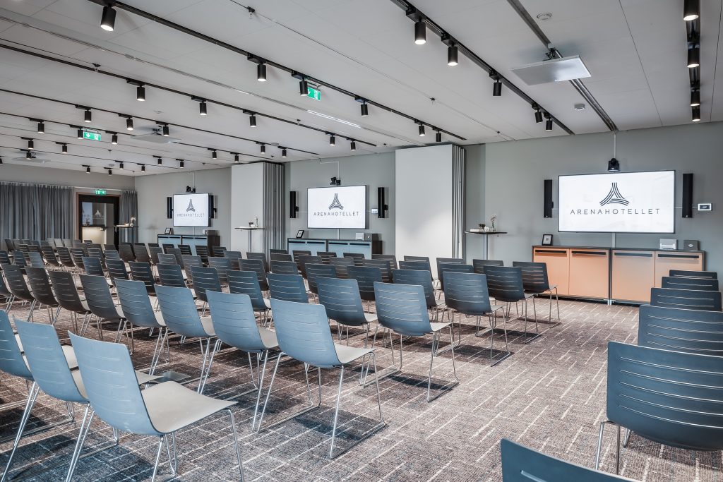 Stort konferensrum med flera rader stolar och tre skärmar