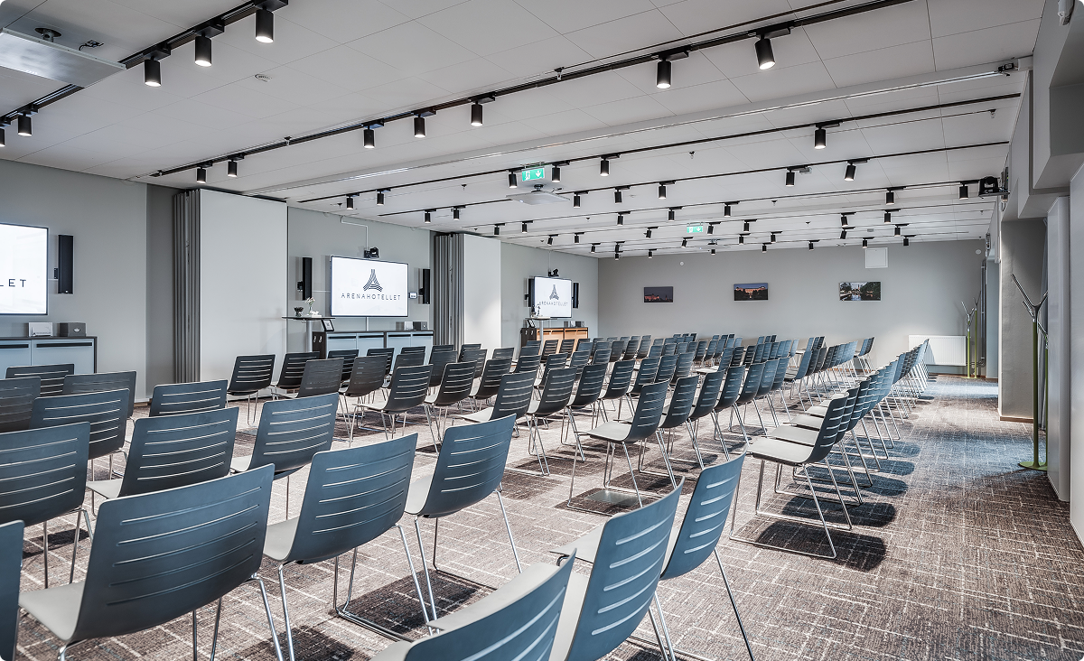 Stort konferensrum med flera rader stolar och tre skärmar