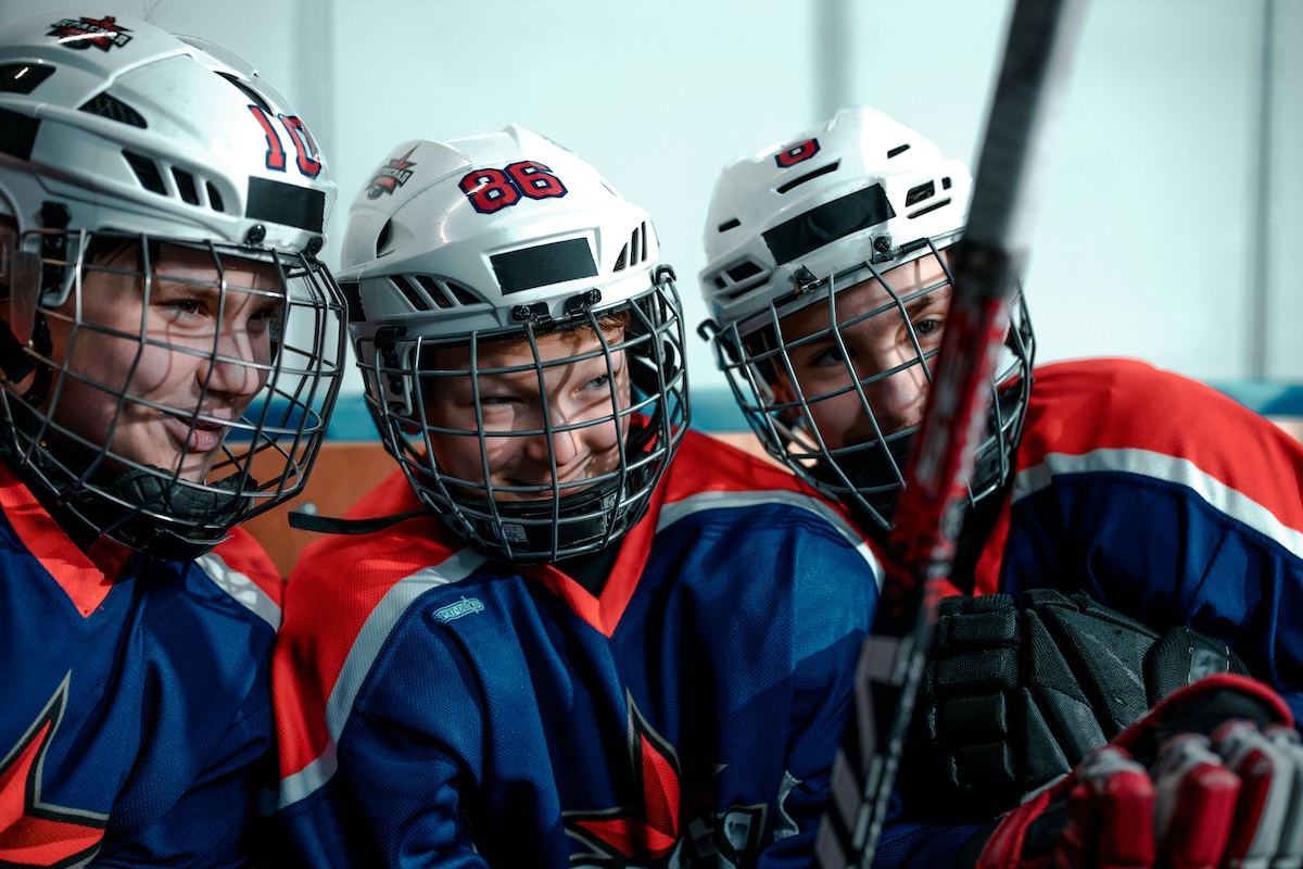 Tre barn i röda och blåa hockeykläder som pratar med varandra